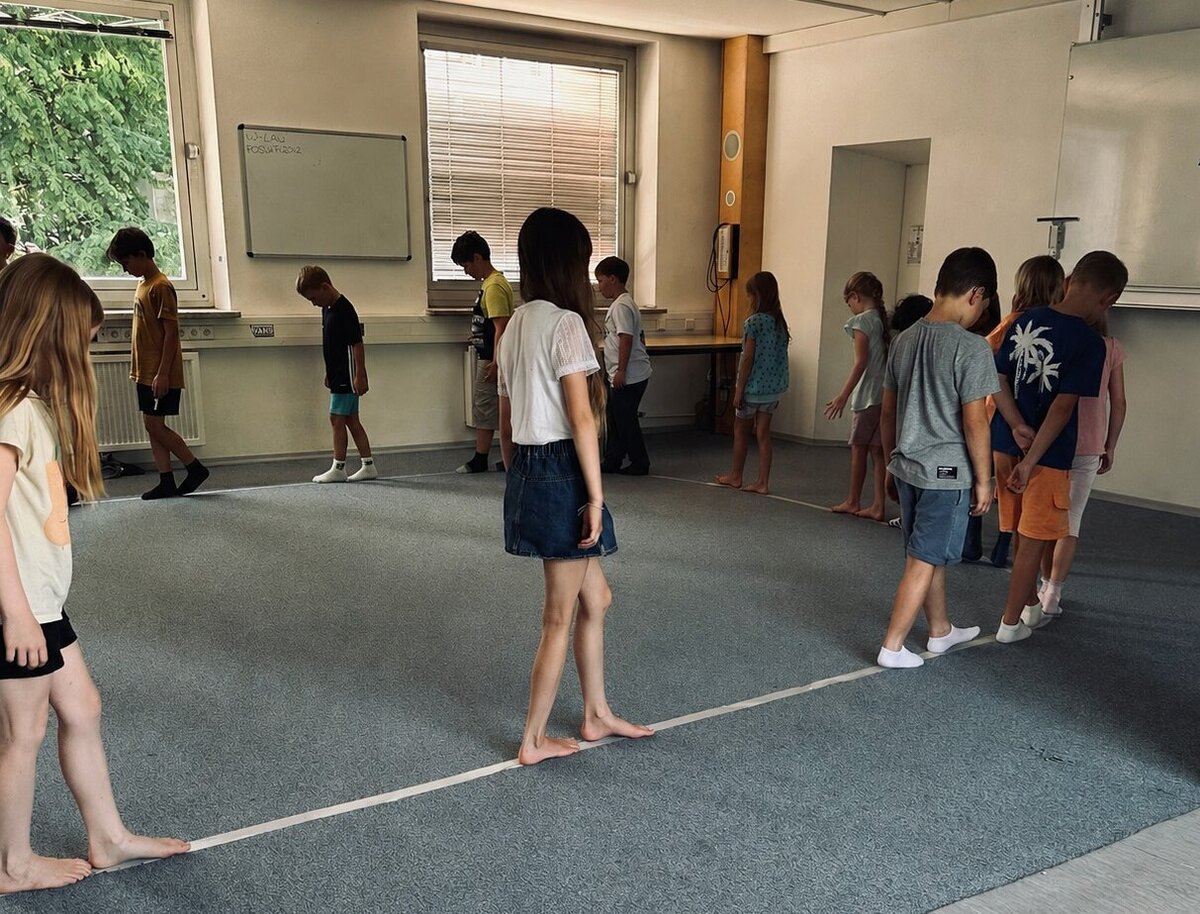 einige Grundschulkinder gehen, jeweils mit etwas Abstand, auf einer Linie